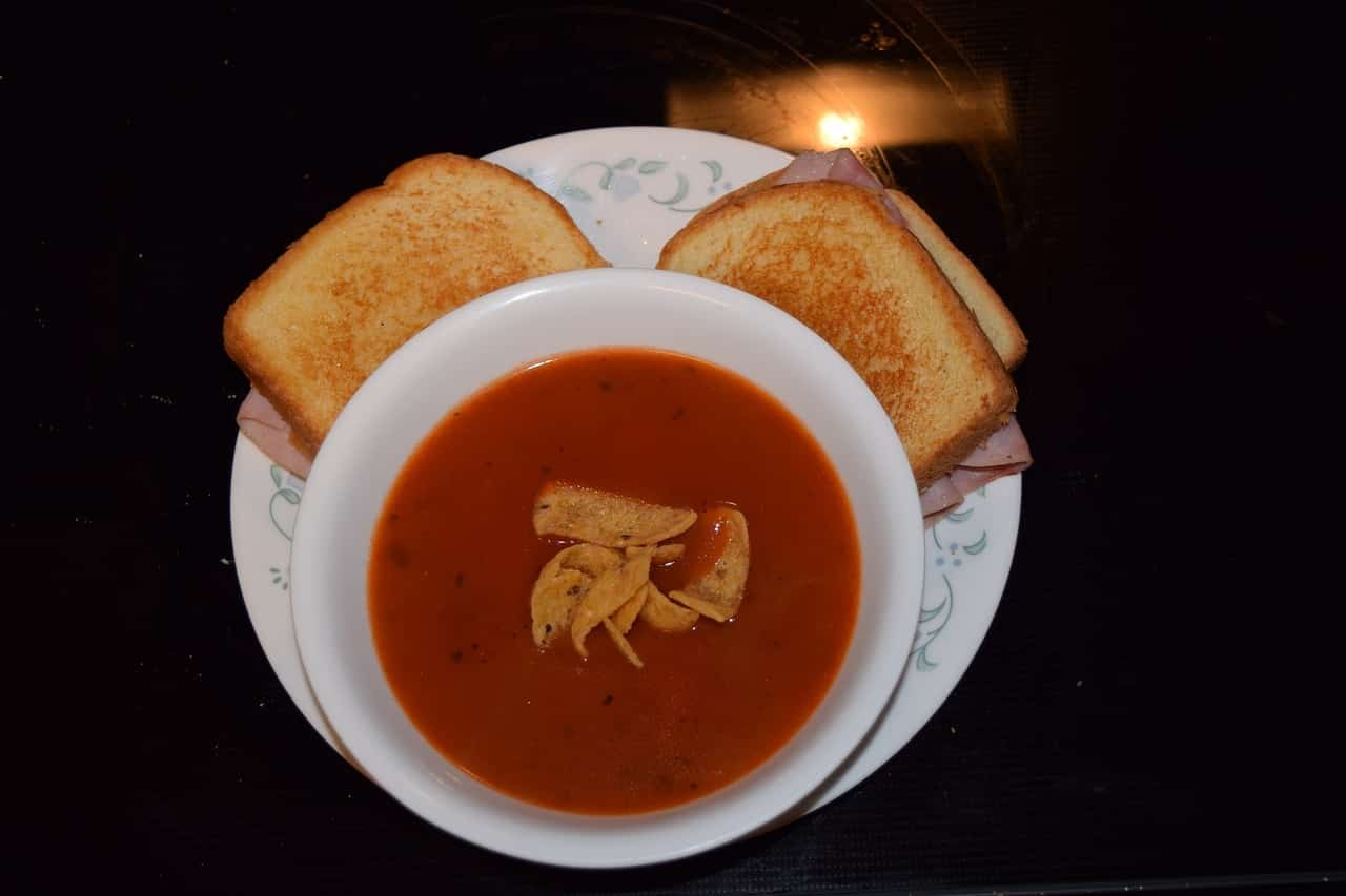 A bowl of tomato soup with a grilled cheese sandwich on the side